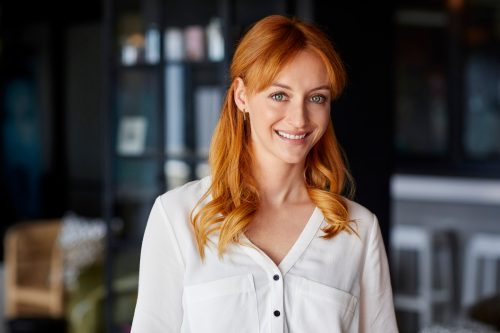 A young pretty woman with red hair smiling at the camera, wearing a white blouse