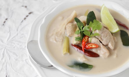 A bowl of tom kha gai, a creamy Thai chicken and coconut soup, on a white surface.