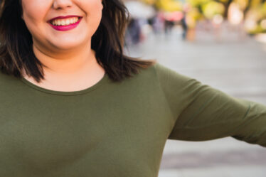 Woman with large bust smiles outside.