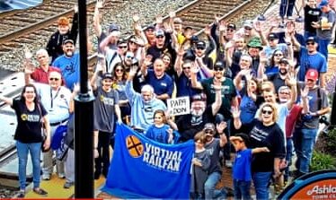 happy people wave at camera. one person holds banner saying ‘virtual railfan’