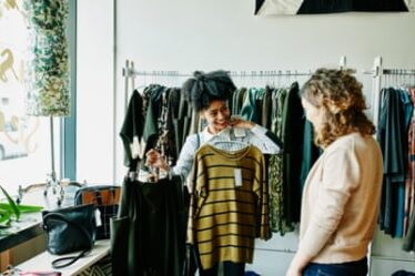 Smiling woman showing shop owner clothing options in boutique shop