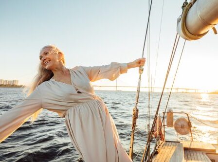 Cheerful senior woman in long dress enjoying vacation on private sailboat