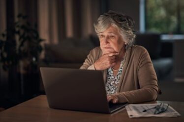 Older woman sitting at her laptop in a dimly lit room