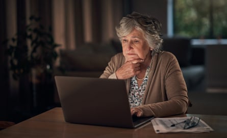 Older woman sitting at her laptop in a dimly lit room