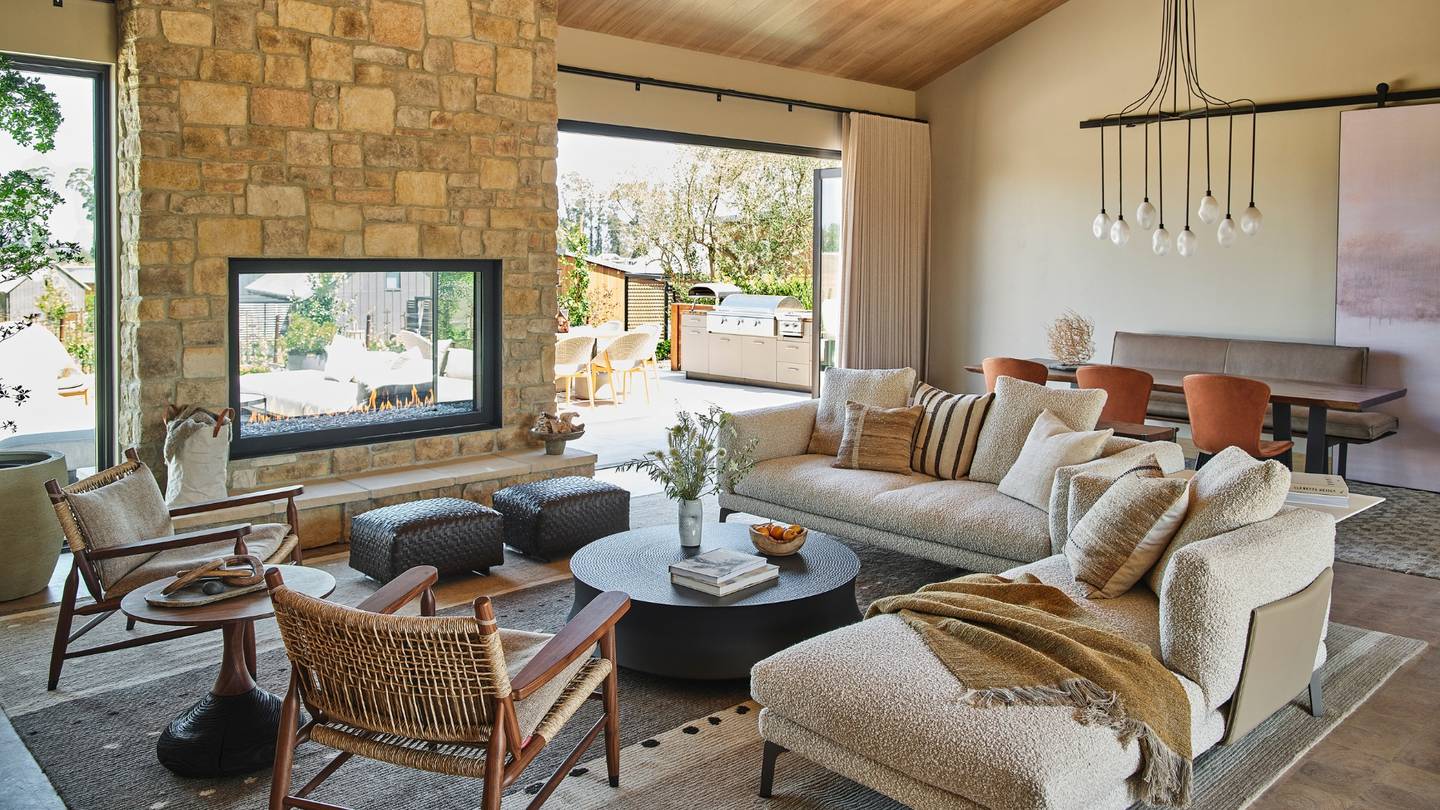 A corner sofa and two chairs stand in the centre of a room filled with natural light and a neutral colour palette.