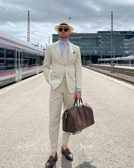 man in a white suit carrying a weekend bag