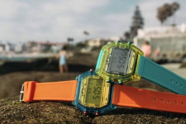 Two digital watches on rocks outside, one is orange and one is blue
