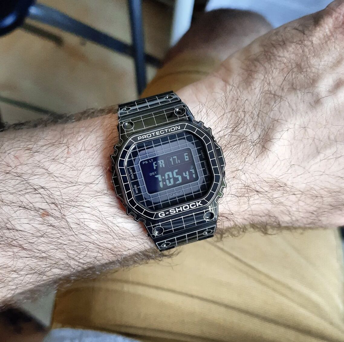 black digital watch on a mans wrist, thigh and floor in the background