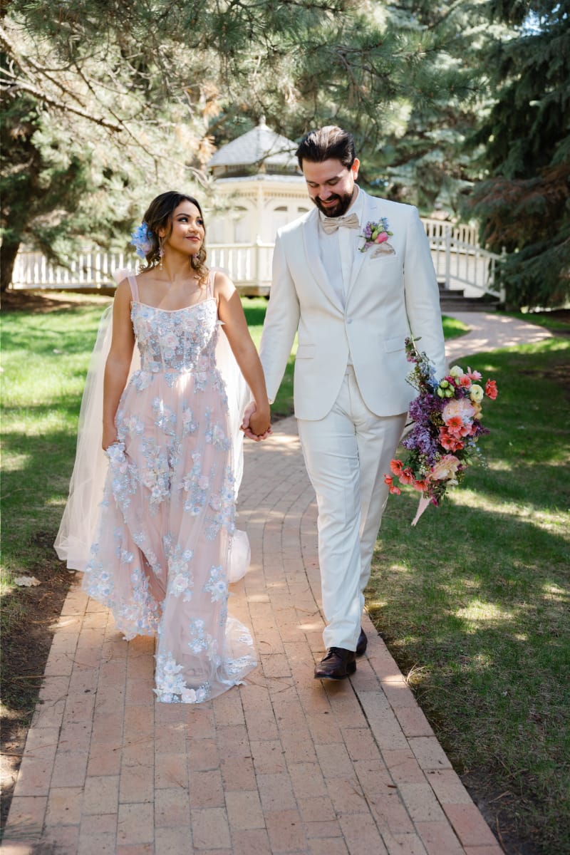 Couple wearing bridal attire walks together outside. 