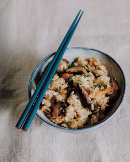 A bowl of rice with mushrooms, chicken and julienned carrots, with a pair of blue chopsticks resting on top