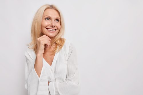 Portrait of a smiling blonde woman wearing a while blouse against a white background.