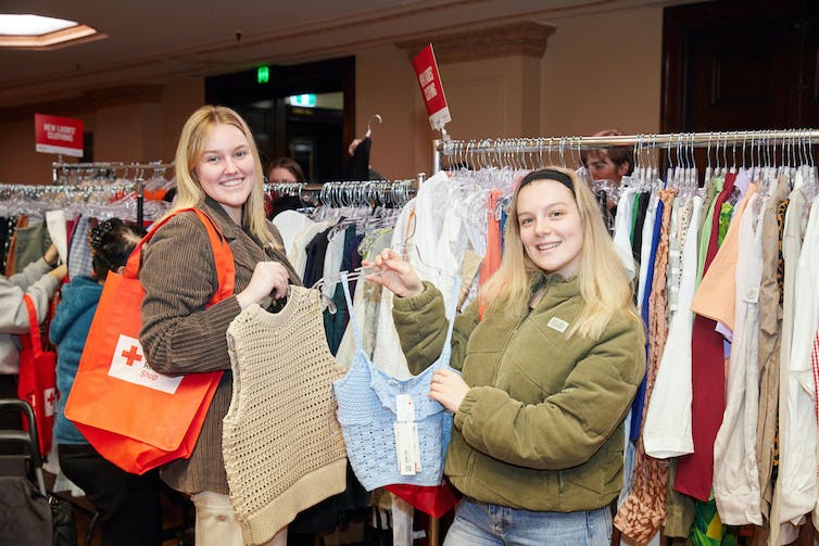 Two young women look at clothes in a Red Cross op shop.