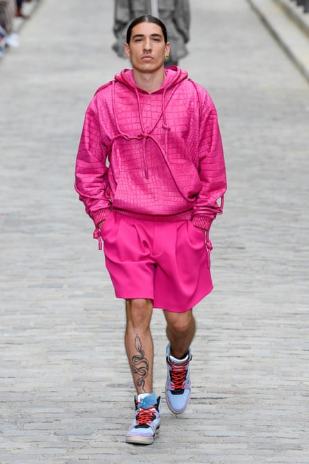 Hector Bellerín with his hands in his pockets on the catwalk, wearing a bright pink designer hoodie and matching pink shorts