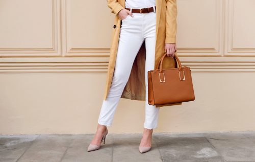 Close up of woman's legs with trendy outfit: white jeans, brown belt, and leather purse