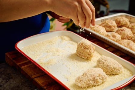 A hand sprinkling panko crumbs on to a chicken rissole