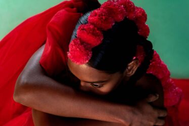 A model with floating red drapery in front of a green backdrop covers her shoulders.