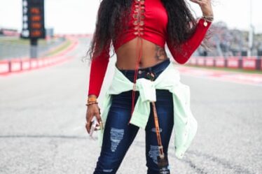 Sha’Carri Richardson in a red long-sleeved crop top and jeans, with a pale green top tied round her waist and long hair with a striped hairband