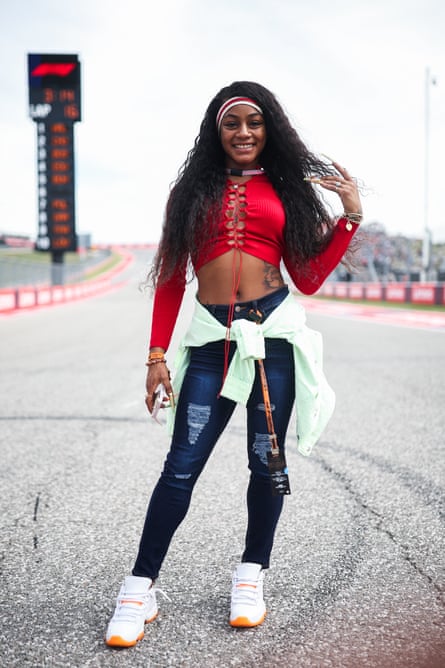 Sha’Carri Richardson in a red long-sleeved crop top and jeans, with a pale green top tied round her waist and long hair with a striped hairband