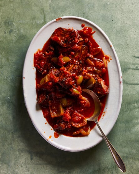 An oval dish set on a marbled green surface, filled with red tomato sauce, onion, and fried eggplant slices.