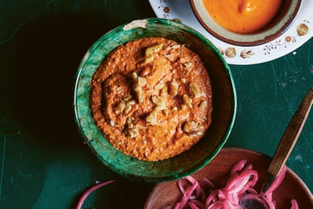 An emerald-green bowl holding an orange-red paste of red capsicum and walnuts, set beside a plate of pickled red onion and a bowl of another bright orange-red sauce.