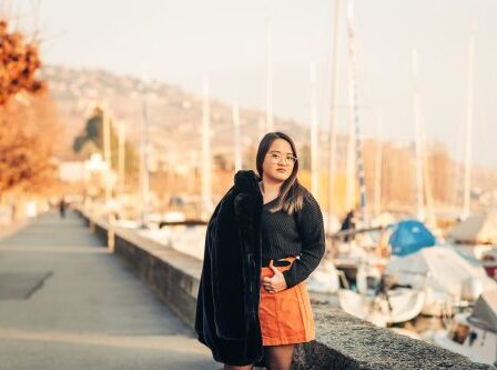 Asian woman with glasses, black faux fur coat and orange skirt