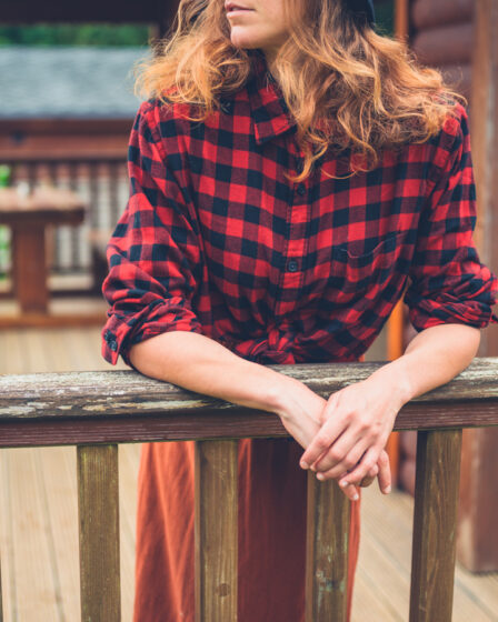 A young woman is relaxing on the porch of a log cabin in the country