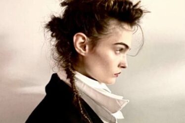 A woman photographed in profile in an old fashioned high-collar outfit with hair messily tied in a top knot and a long ponytail