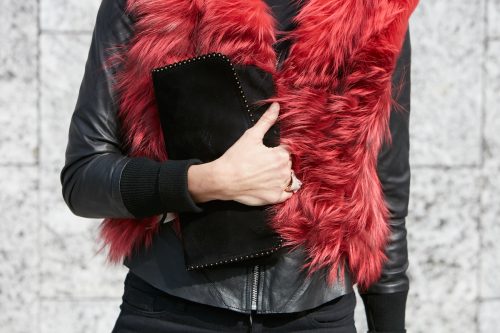 Close up of a woman wearing a black leather jacket and a red fur stole, holding a black clutch.