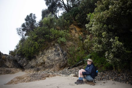 Alison Lester seated on a rock on the beach, gazing out towards the ocean