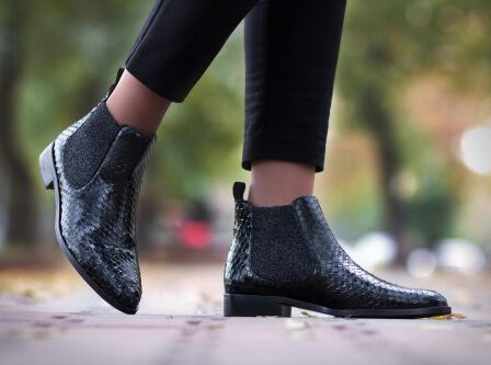 Close up of a woman's legs walking along the street in black python ankle boots.