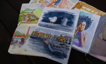A sketchbook sits on top of a pile of other sketchbooks, with a seagull painted on one page and boards in a harbour on another.