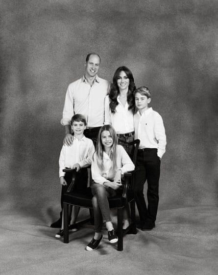 full-length portrait format version of the photograph showing Louis and Charlotte wearing white-toed sneakers; Charlotte is seated in a chair in front of her parents and brothers and is wearing jeans, with her long fair hair loose. Catherine is wearing denim jeans, William and George have black trousers, while Louis appears to be wearing dark shorts.