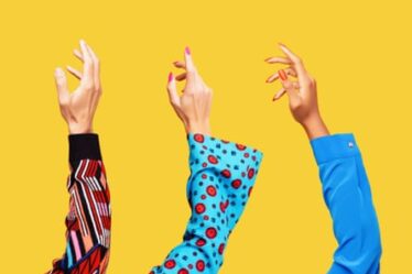 Hands of a white man, a white woman and a black woman reaching up into the air shot on yellow background.