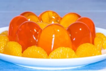 A large orange jelly, surrounded by segments of orange, standing on a plate