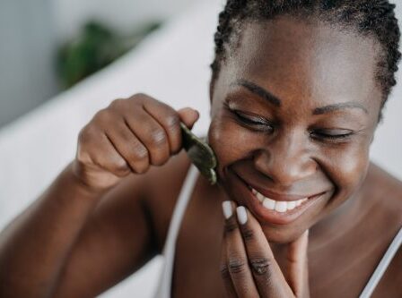 Close up of a smiling woman using a gua sha tool on her face