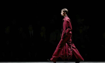 A model on the Gucci catwalk wearing a red suit and carrying a bag. 