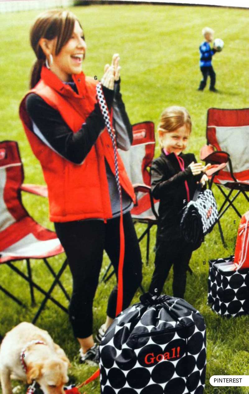 Joyful soccer mom with child and dog at a soccer game, with chairs and gear.