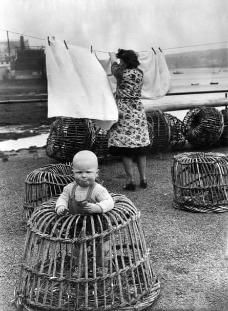 A 14-month-old baby, David, contained in a lobster pot while his mother hangs the washing