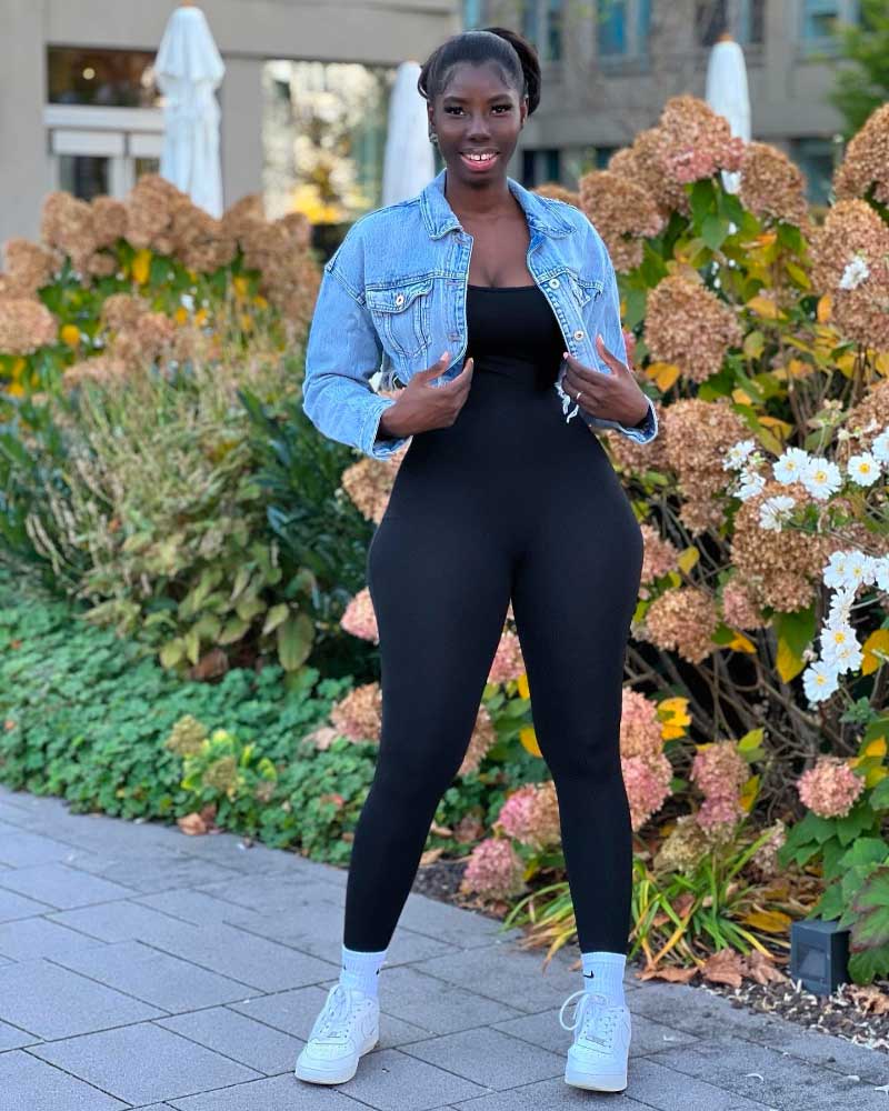 Confident woman in a casual black bodysuit and denim jacket outdoors