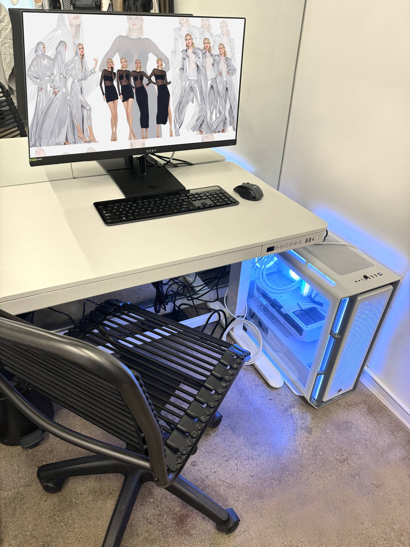 A computer with a glowing blue light sits in the corner of an office next to a desk with a monitor showing Kamali's designs.