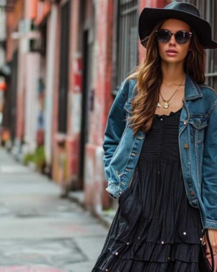 Stylish urban outfit with black maxi dress, denim jacket, and wide-brimmed hat.