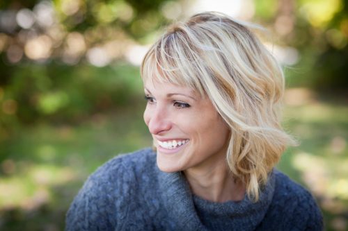 Smiling, middle-aged woman with a blonde bob haircut and a blue sweater outside