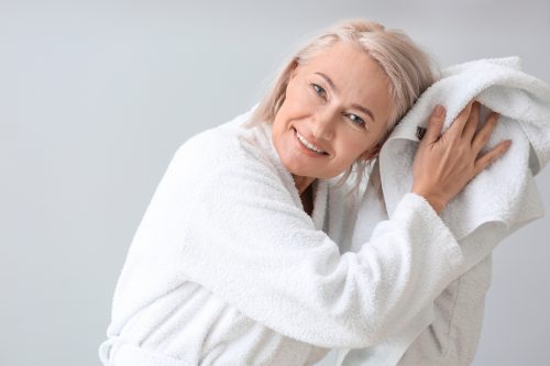 Happy mature woman in bathrobe and with towel on grey background