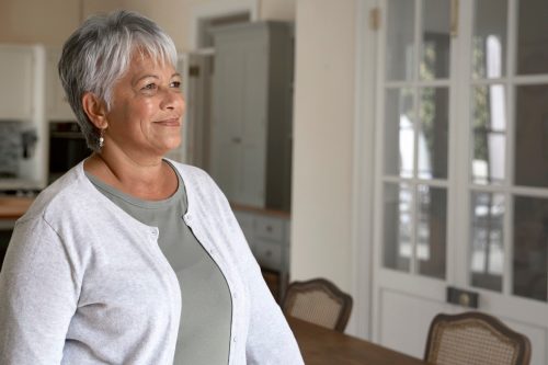 Side view portrait of of a mature woman in her kitchen. She has short gray hair and is wearing a gray t-shirt with a white cardigan.