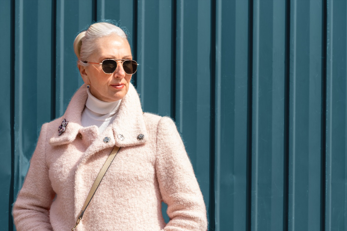 Chic Older Woman in Sunglasses and Pink coat against a teal wall