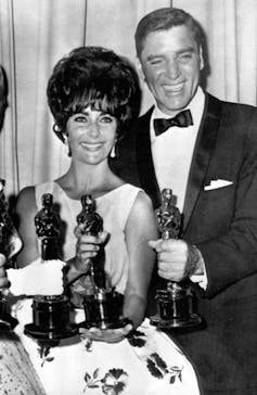 People holding Oscar trophies, one in a dress and one in a tuxedo.