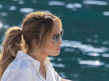 Side profile of Jennifer Lopez wearing a white shirt on the water. Her hair is pulled back into a ponytail and she's wearing sunglasses.