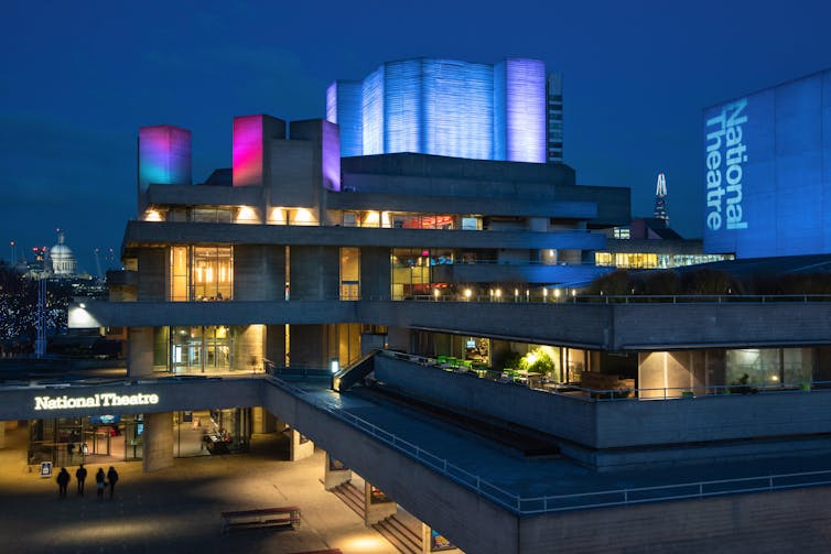A concrete building on London's South Bank - the National Theatre - illuminated in red and blue at night.