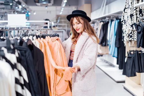 Fashion woman customer looking on peach color shirt in store. Buying clothes using fitting concept while choosing, professional stylist creating trendy look according to color of the 2024 year