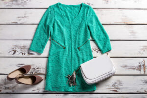 Turquoise dress with white purse and brown heels on a white wood background